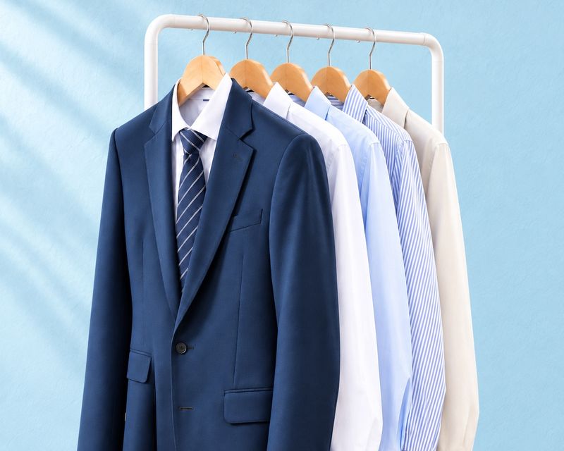 A navy suit and pressed dress shirts on wooden hangers